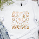 White t-shirt with gold text design on a wooden surface with denim jeans and headphones.