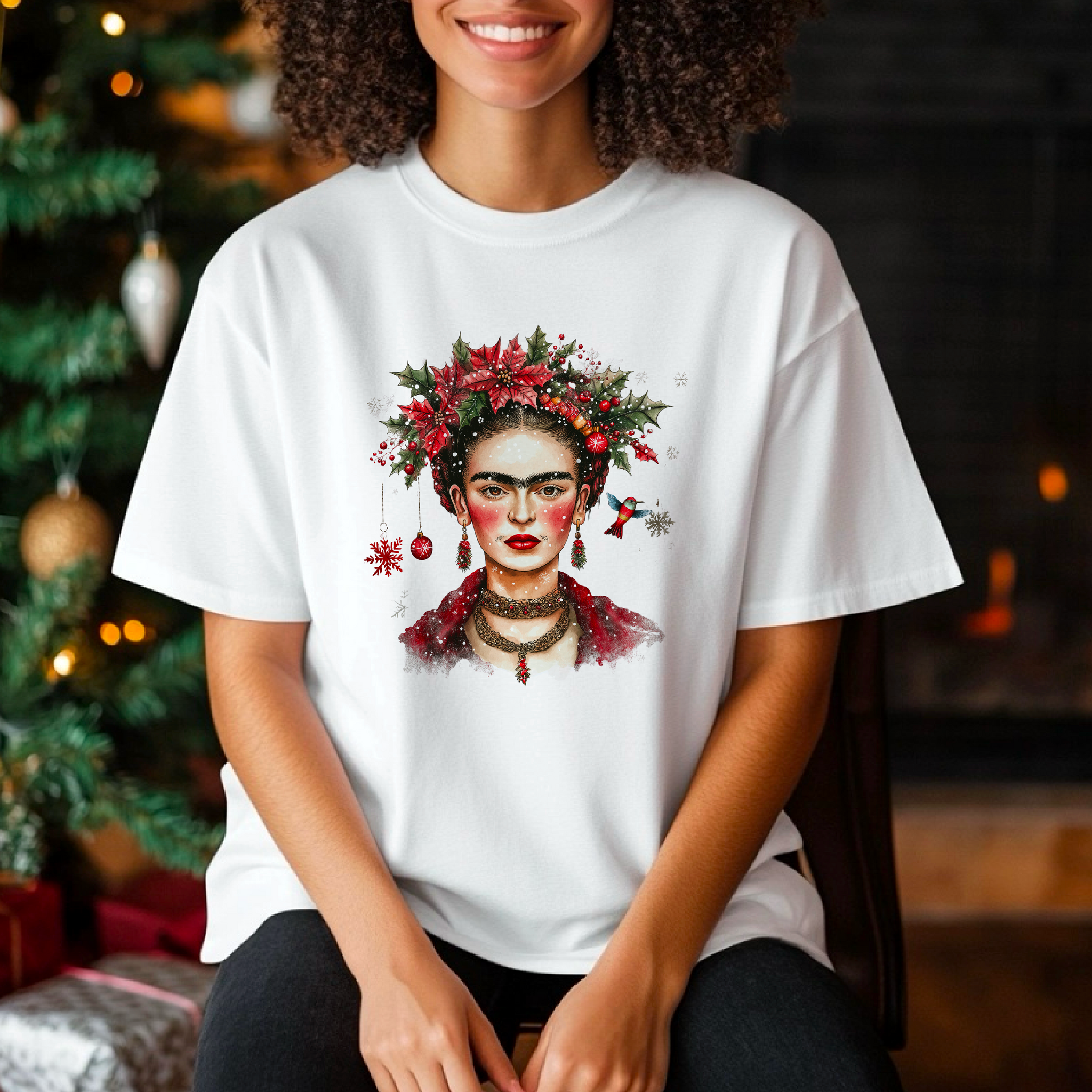 Person wearing a white t-shirt with a Frida Kahlo design in a festive setting with a Christmas tree and fireplace.