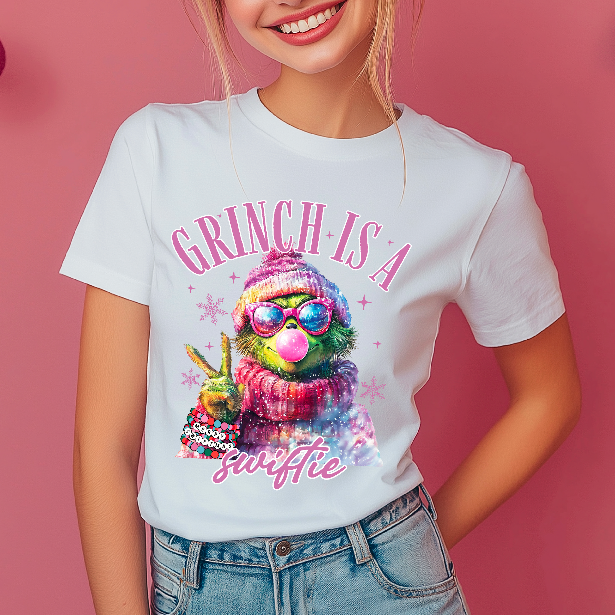 A person wearing a white crew neck t-shirt with a graphic print of the Grinch character, surrounded by Christmas-themed decorations.