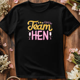 Black t-shirt with 'Team Hen' text on a wooden surface with flowers