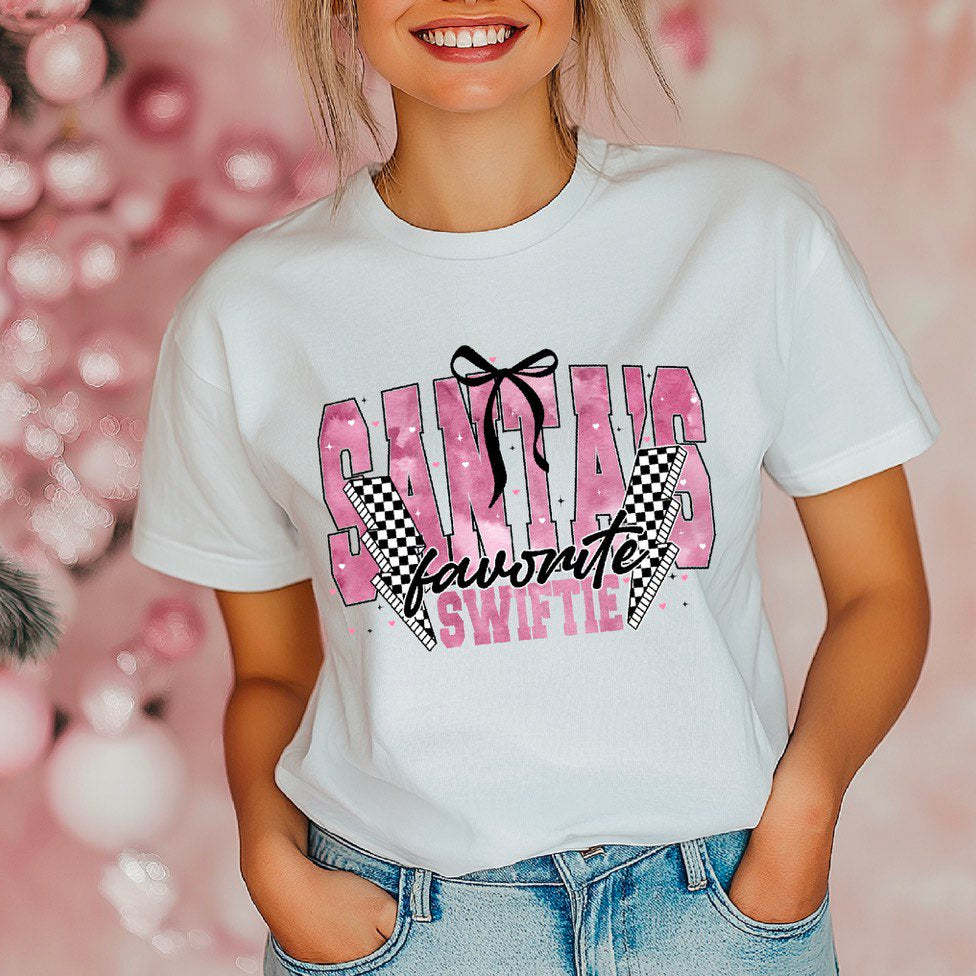 A person wearing a white t-shirt with the text 'SANTA'S FAVORITE SWIFTIE' and a graphic design.